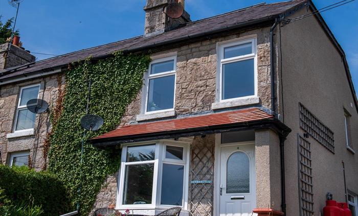 The front of the cottage, there is a driveway with parking on the right